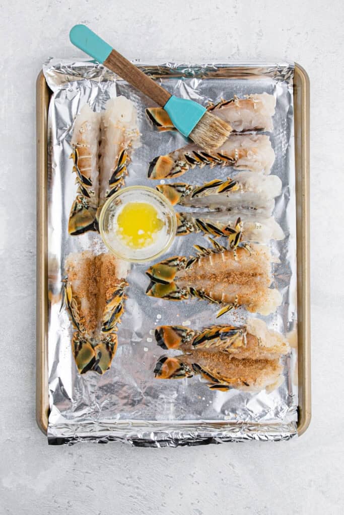 Lobster split on a baking sheet with butter being brushed on top