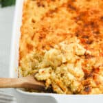 Mac and cheese being lifted from a white casserole dish on white background