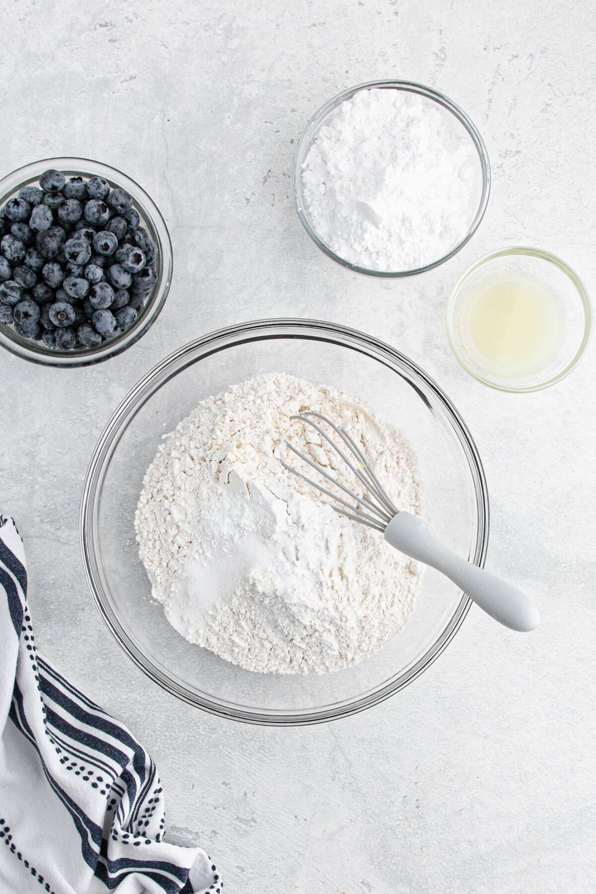 Dry ingredients in a glass bowl with whisk, surrounded by blueberries and lemon juice