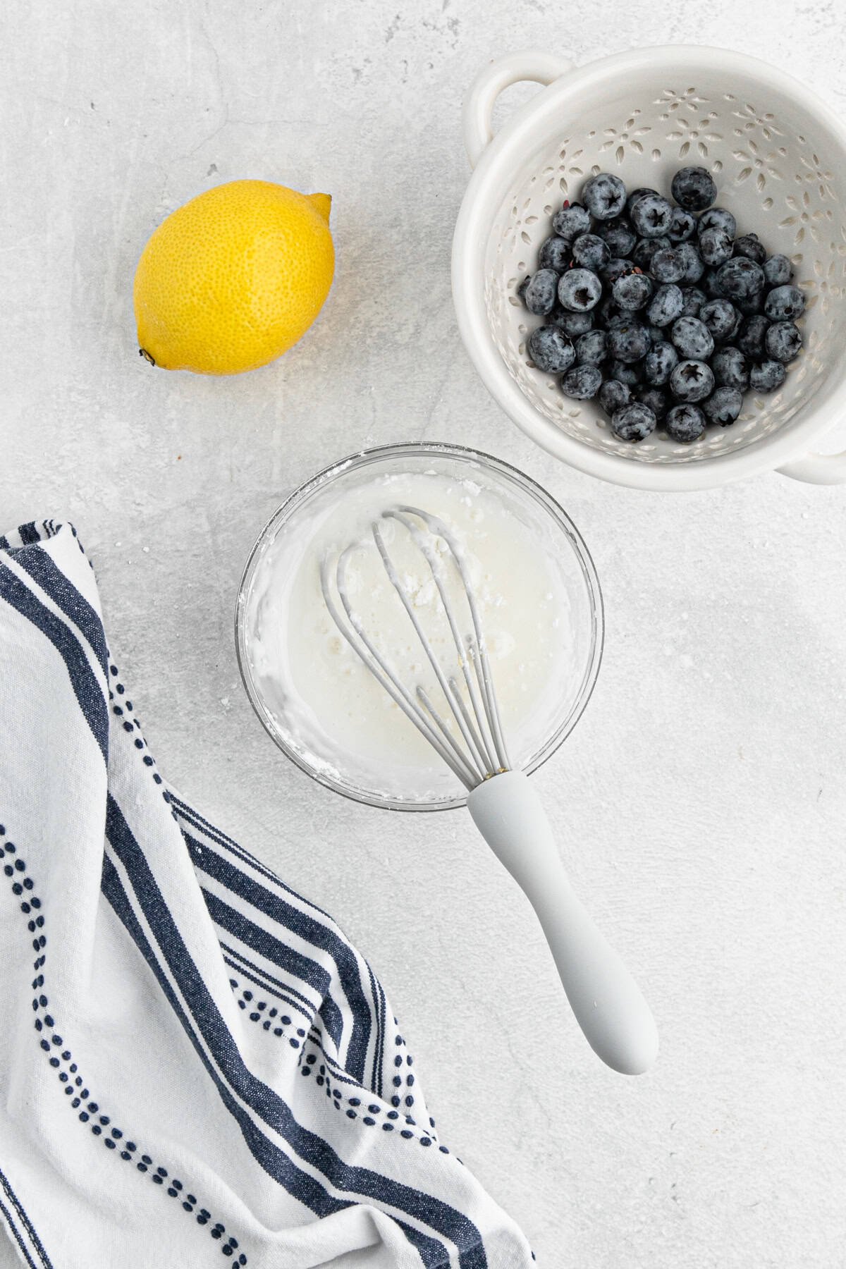 Simple glaze being whisked in a small bowl next to blueberries and a lemon