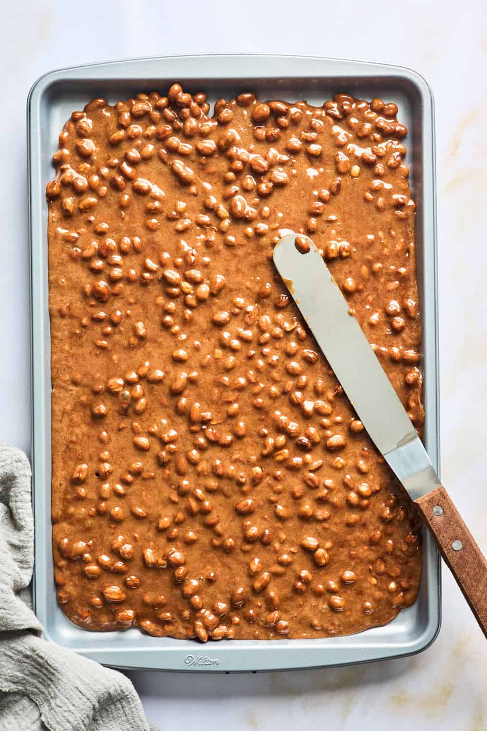 Peanut candy being spread in a sheet pan with a spatula to make smooth