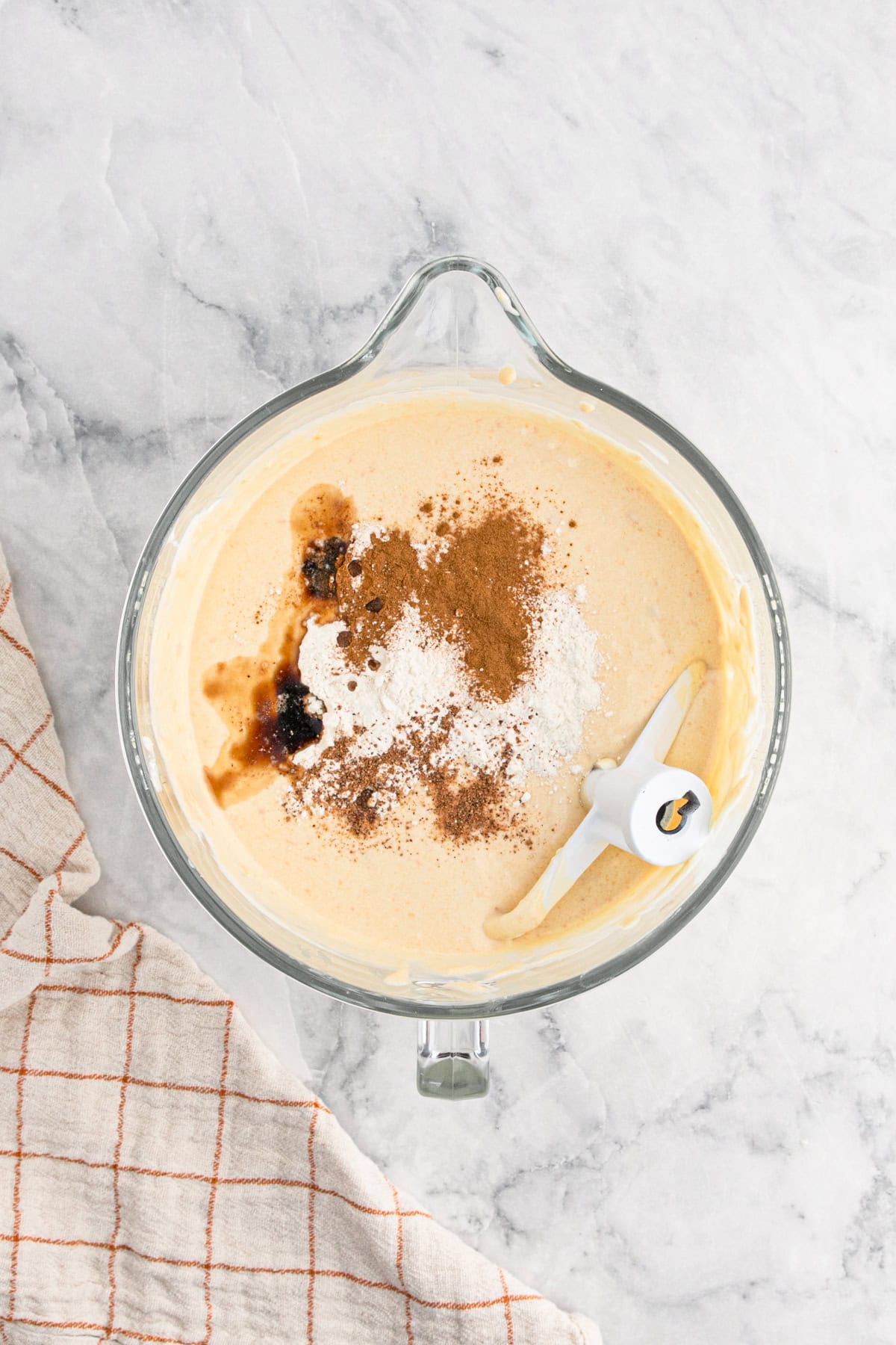 Spices, flour, and vanilla extract sprinkled over the sweet potato cheesecake batter in a bowl