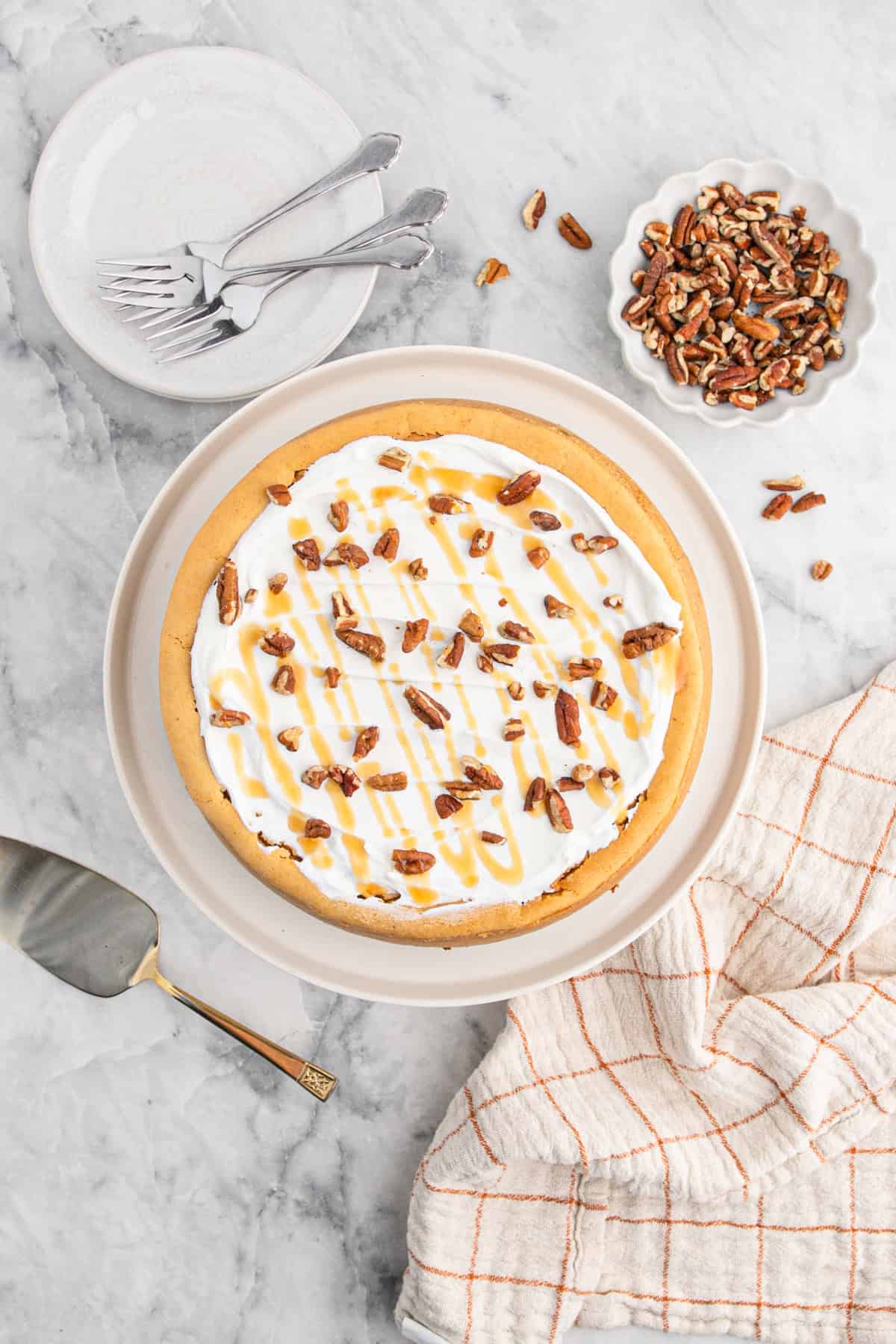 Fully baked and decorated sweet potato cheesecake topped with whipped cream, pecans, and caramel drizzle on a serving plate