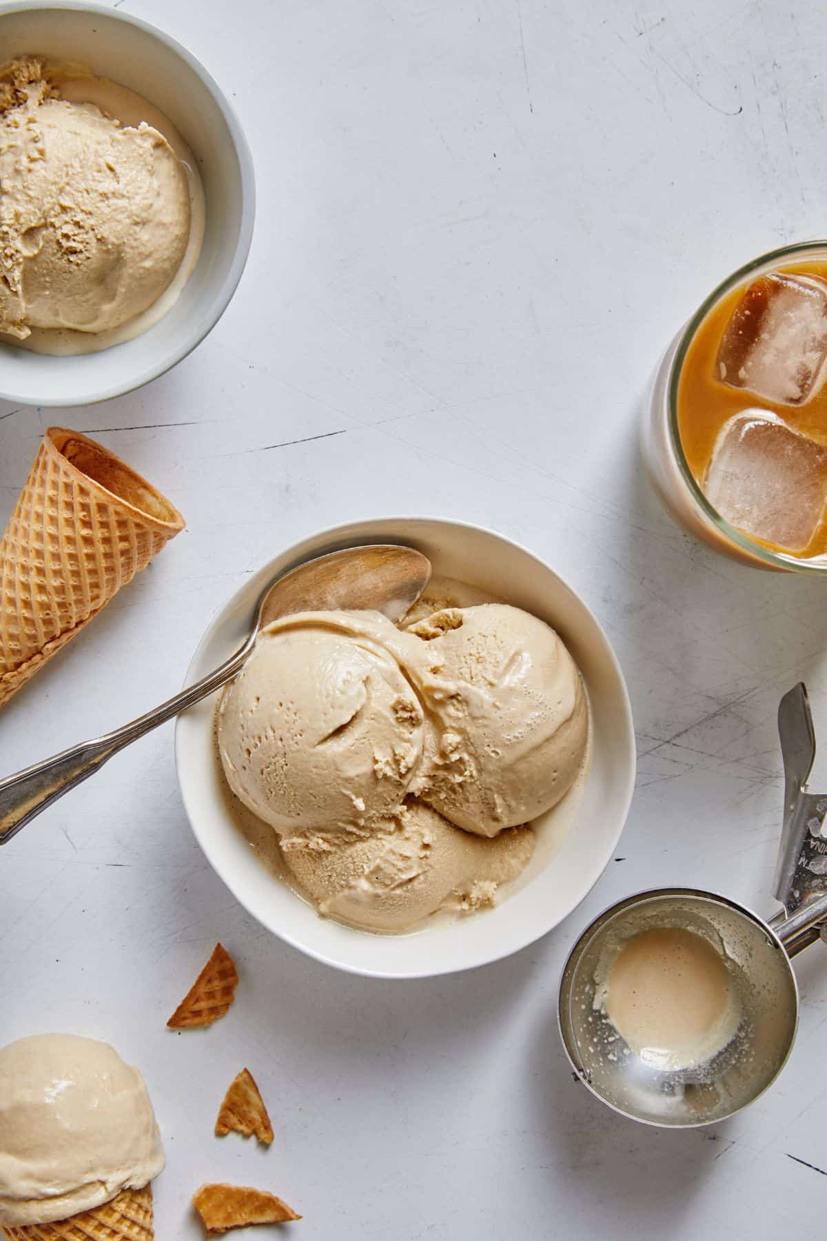 Three scoops of coffee ice cream in a bowl with ice cream cones, a cup of coffee and a scoop of ice cream around it