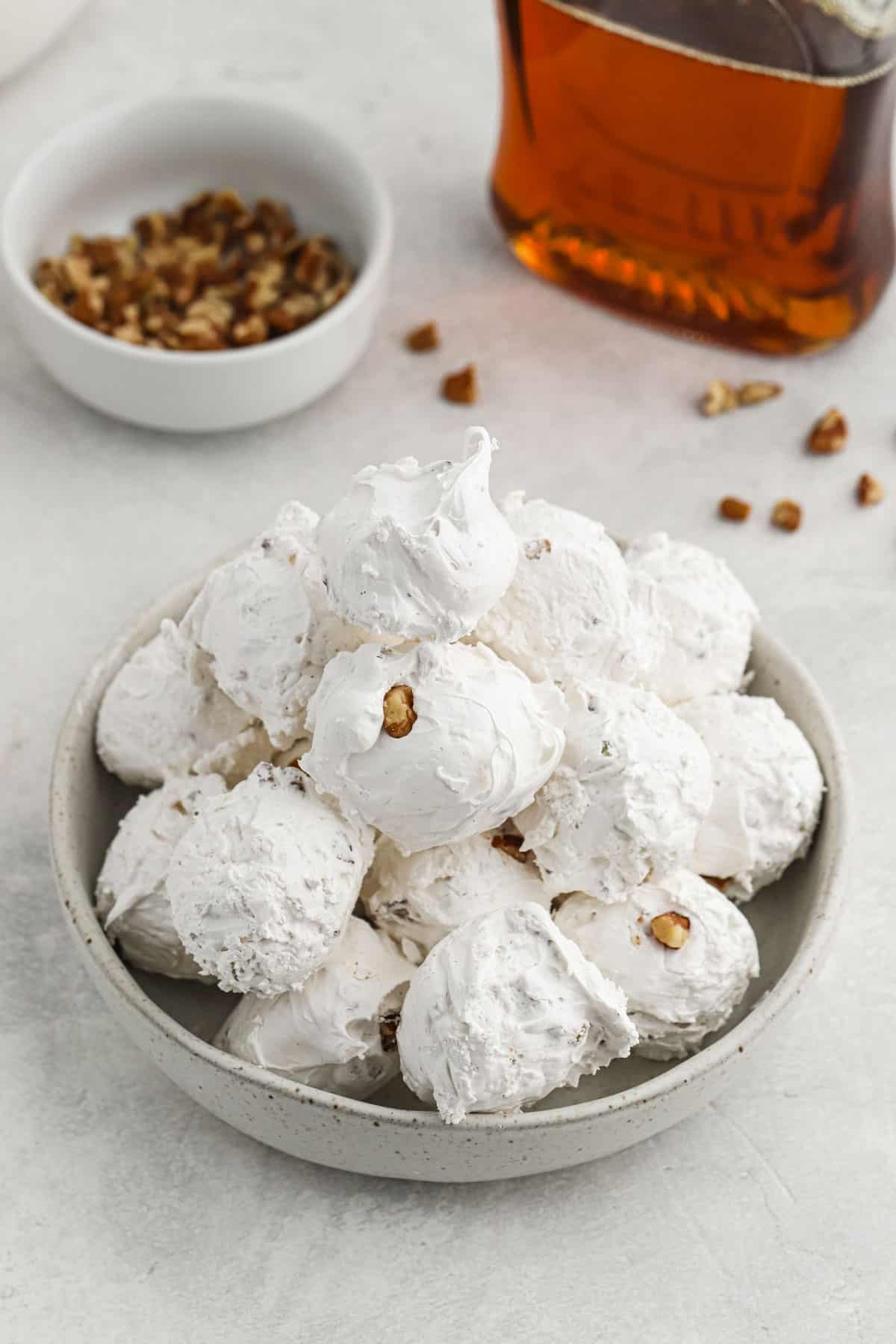 A pile of divinity candy on a grey dish with pecans and a bottle of maple syrup in the background