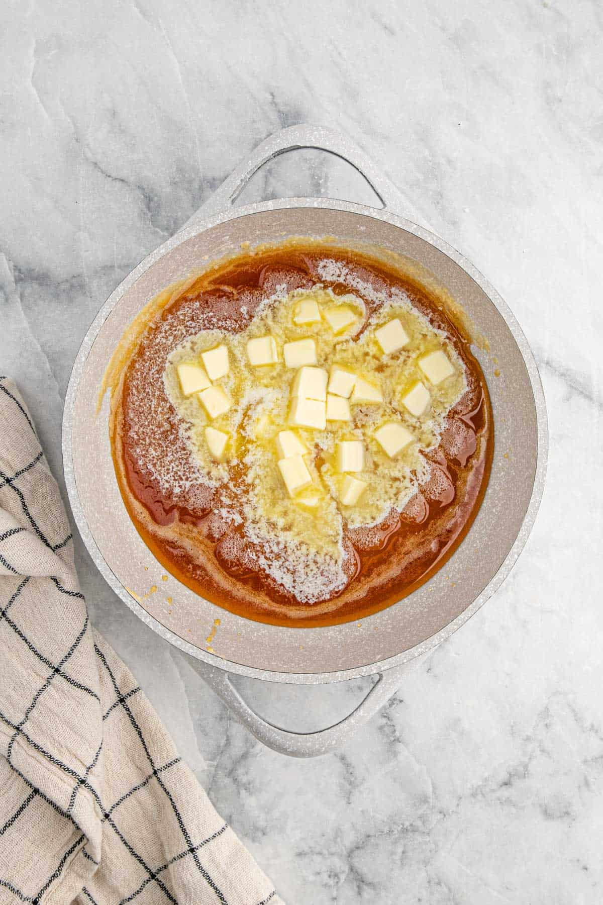A pot of golden-brown caramelized sugar with diced butter slowly melting into it