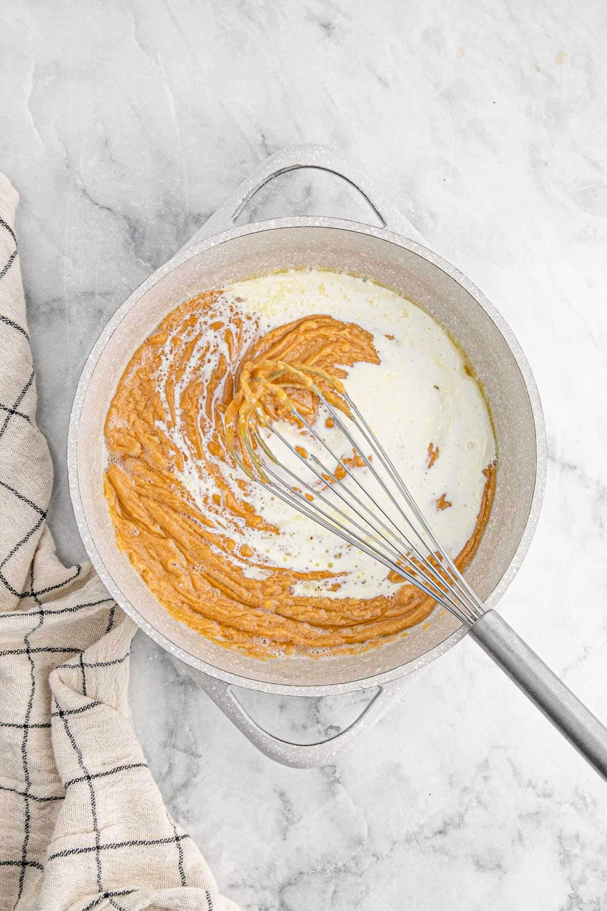 A whisk mixing the caramel sauce with cream in a pot