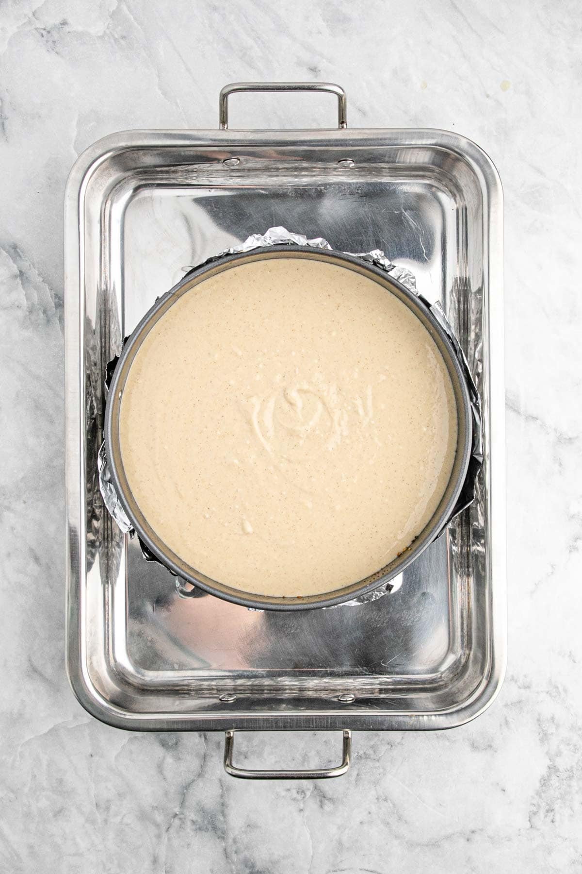 A springform pan filled with cheesecake batter, wrapped in foil and placed in a water bath
