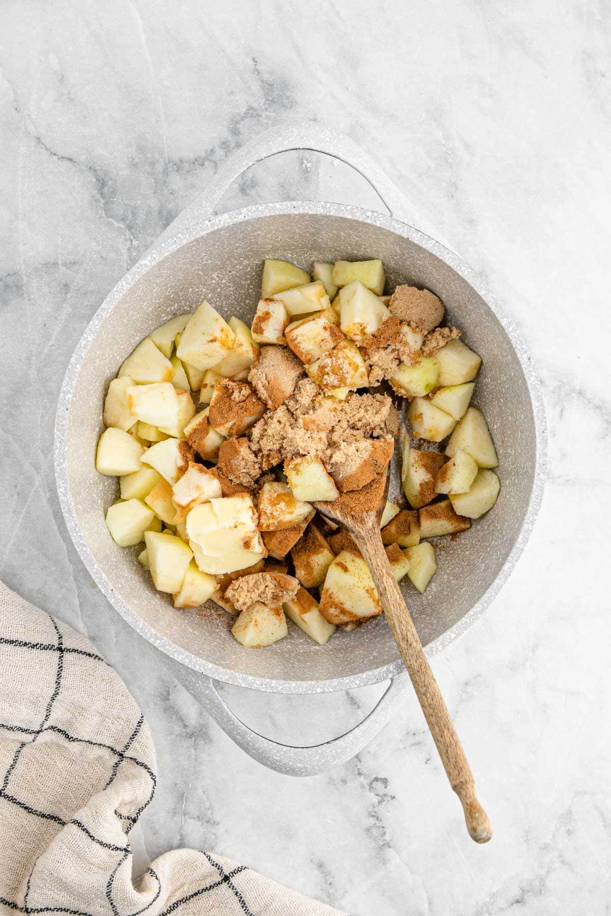 A pot filled with chopped apples, butter, brown sugar, and cinnamon before cooking