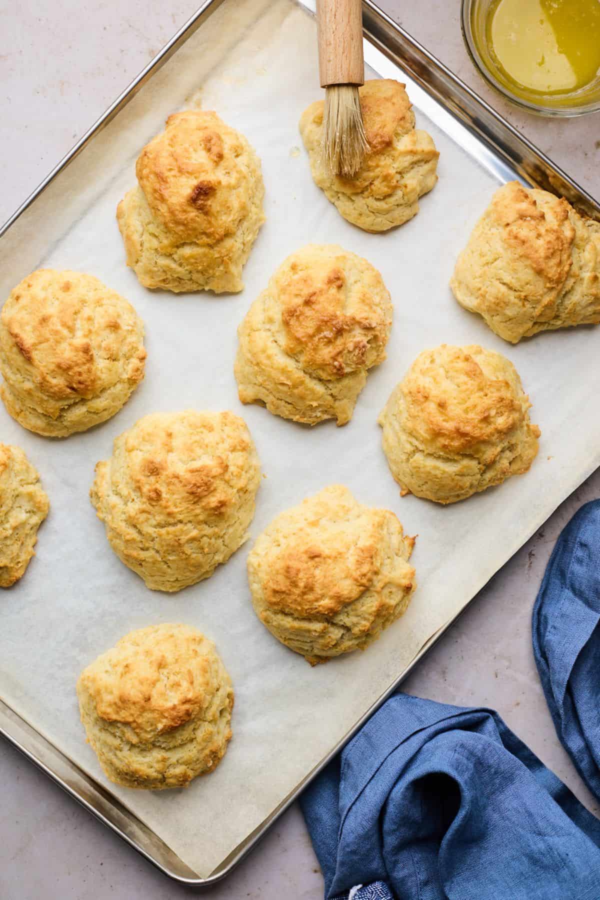 Baked drop biscuits on sheet pan being brushed with butter