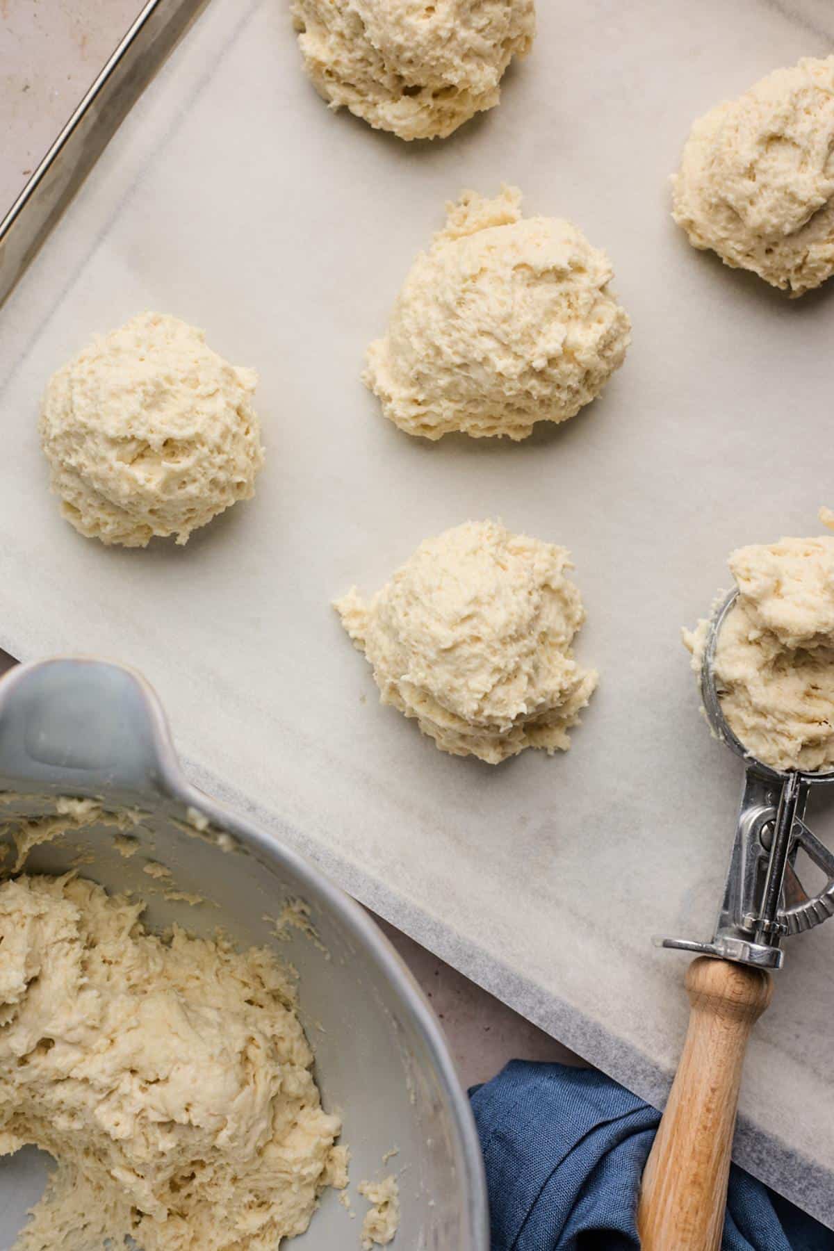 Scoops of biscuit dough on parchment-lined baking sheet