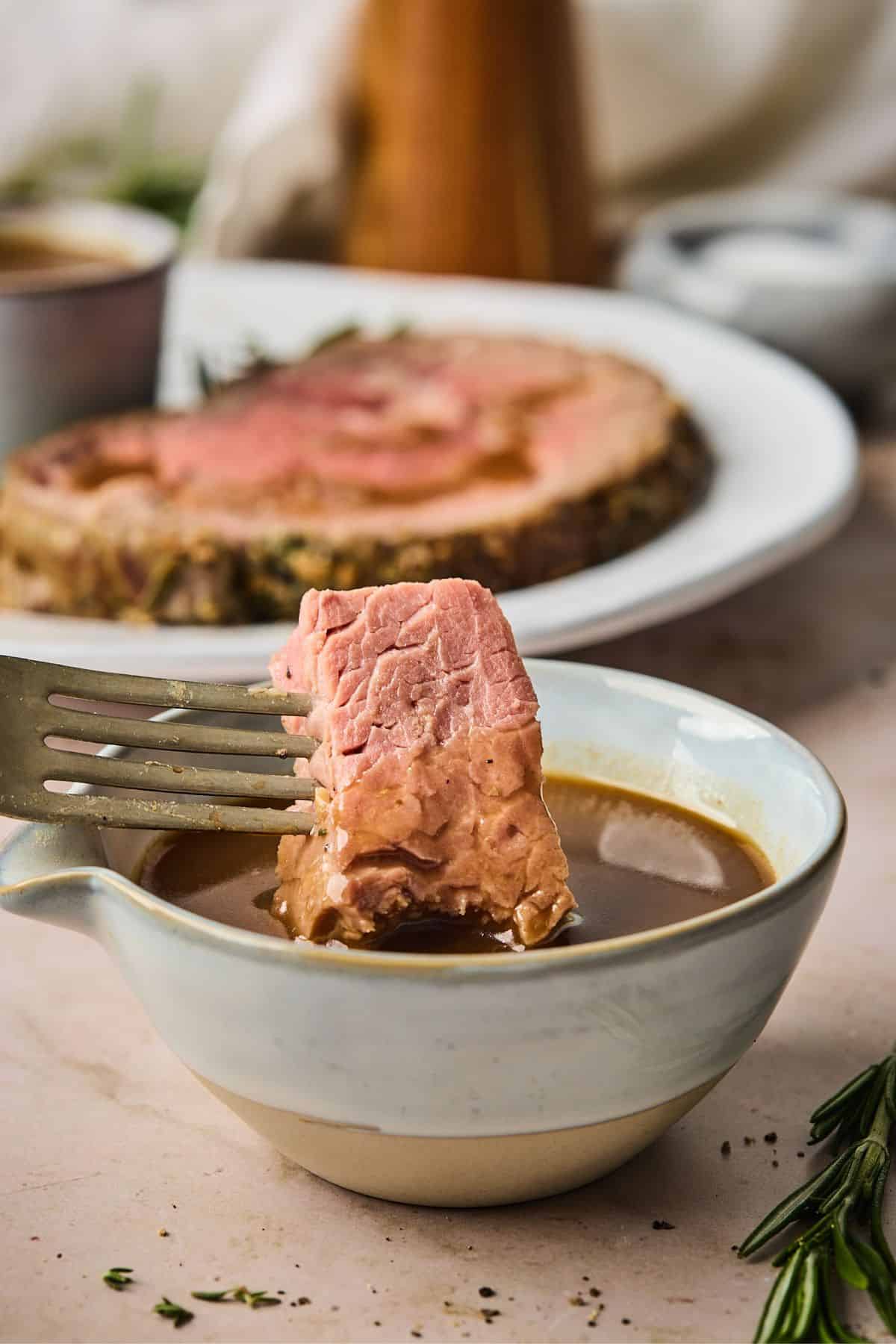 bite of prime rib being dipped in a small bowl full of the best au jus recipe