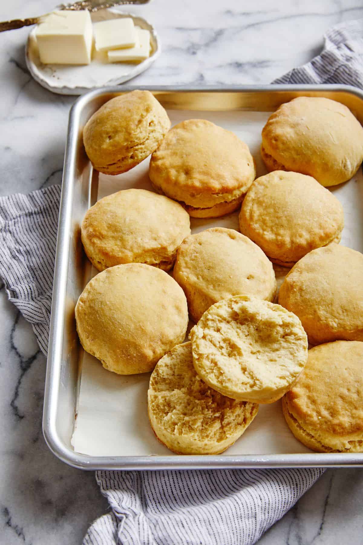 Buttermilk biscuits on a sheet pan with one biscuit cut open in half