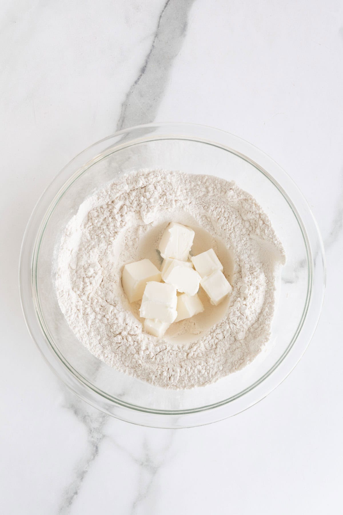 Shortening added to dry ingredients in a glass bowl on countertop