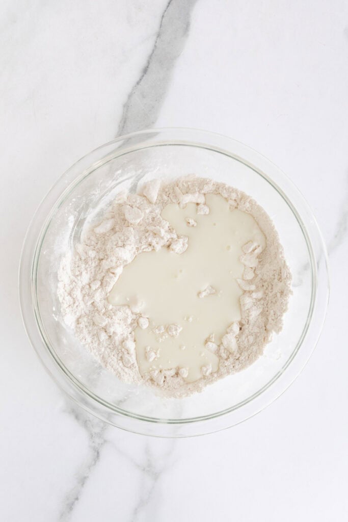 Buttermilk added to shortening mixed flour in a glass bowl