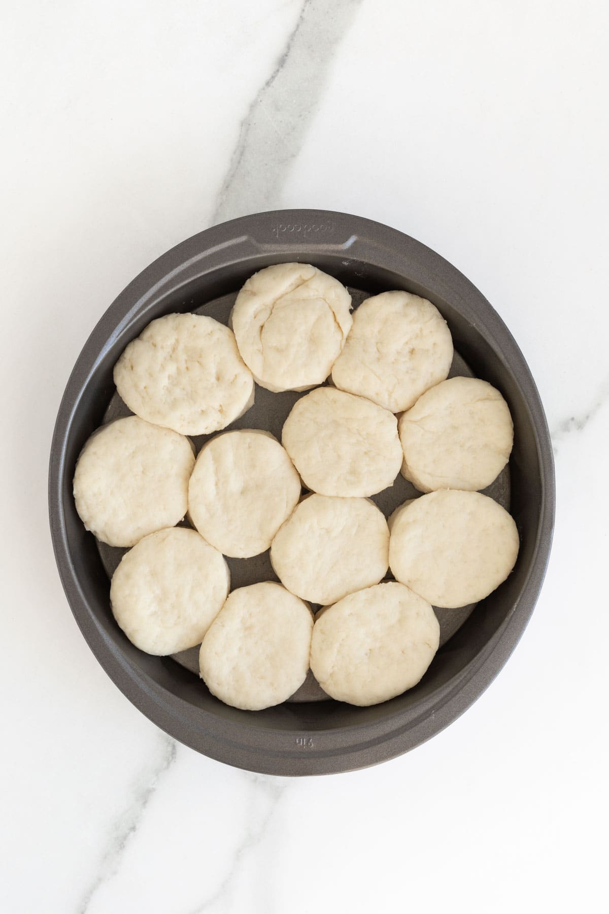 Buttermilk biscuit rounds cut out in a round pan on countertop