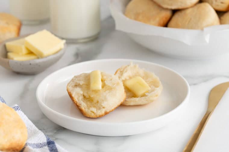 A buttermilk biscuit sliced open with butter added inside on a white plate