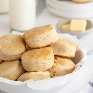 A white platter of buttermilk biscuits with butter and milk in the background