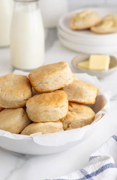 A white platter of buttermilk biscuits with butter and milk in the background