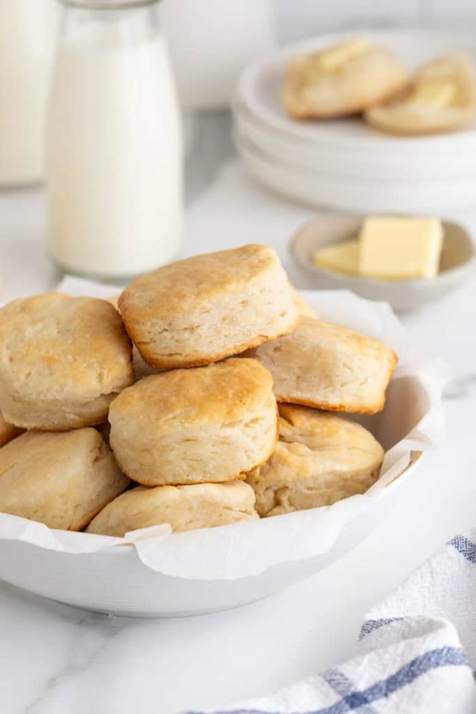 A white platter of buttermilk biscuits with butter and milk in the background