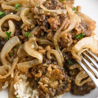 Liver and onions on a white plate with a silver fork piercing some to eat