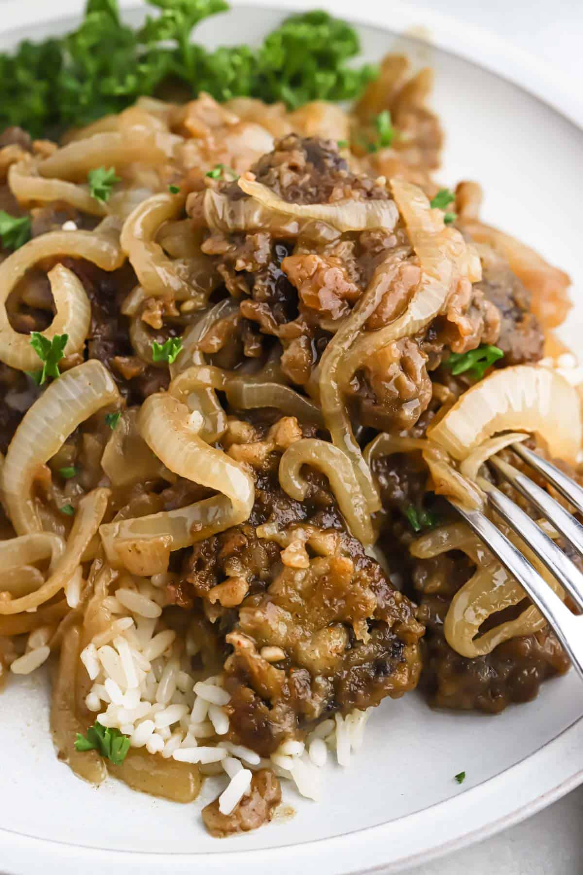 Liver and onion recipe served over white rice on a white plate