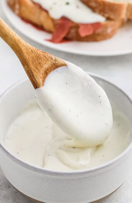 White gravy in a large white bowl with a wooden spoon