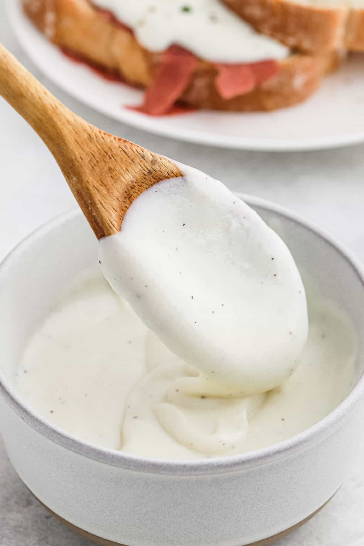 A wooden spoon with a thick creamy gravy drizzling into the pot