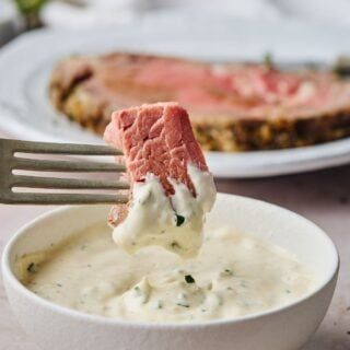 A horseradish sauce in a white bowl with prime rib dipping into it
