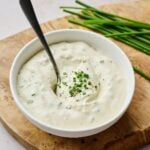 A bowl full of horseradish sauce recipe garnished with chives with a spoon on it