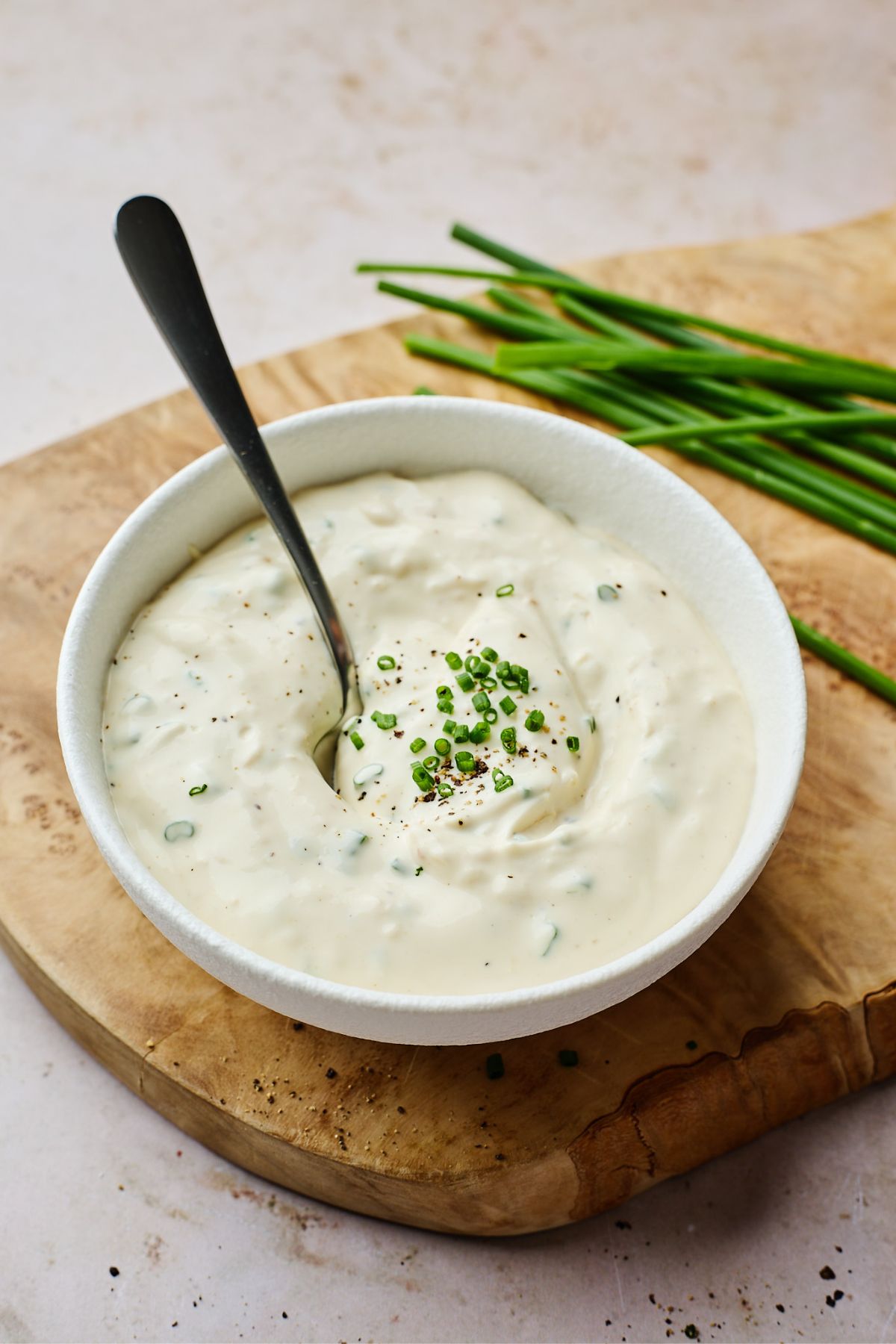 A bowl full of horseradish sauce recipe garnished with chives with a spoon on it