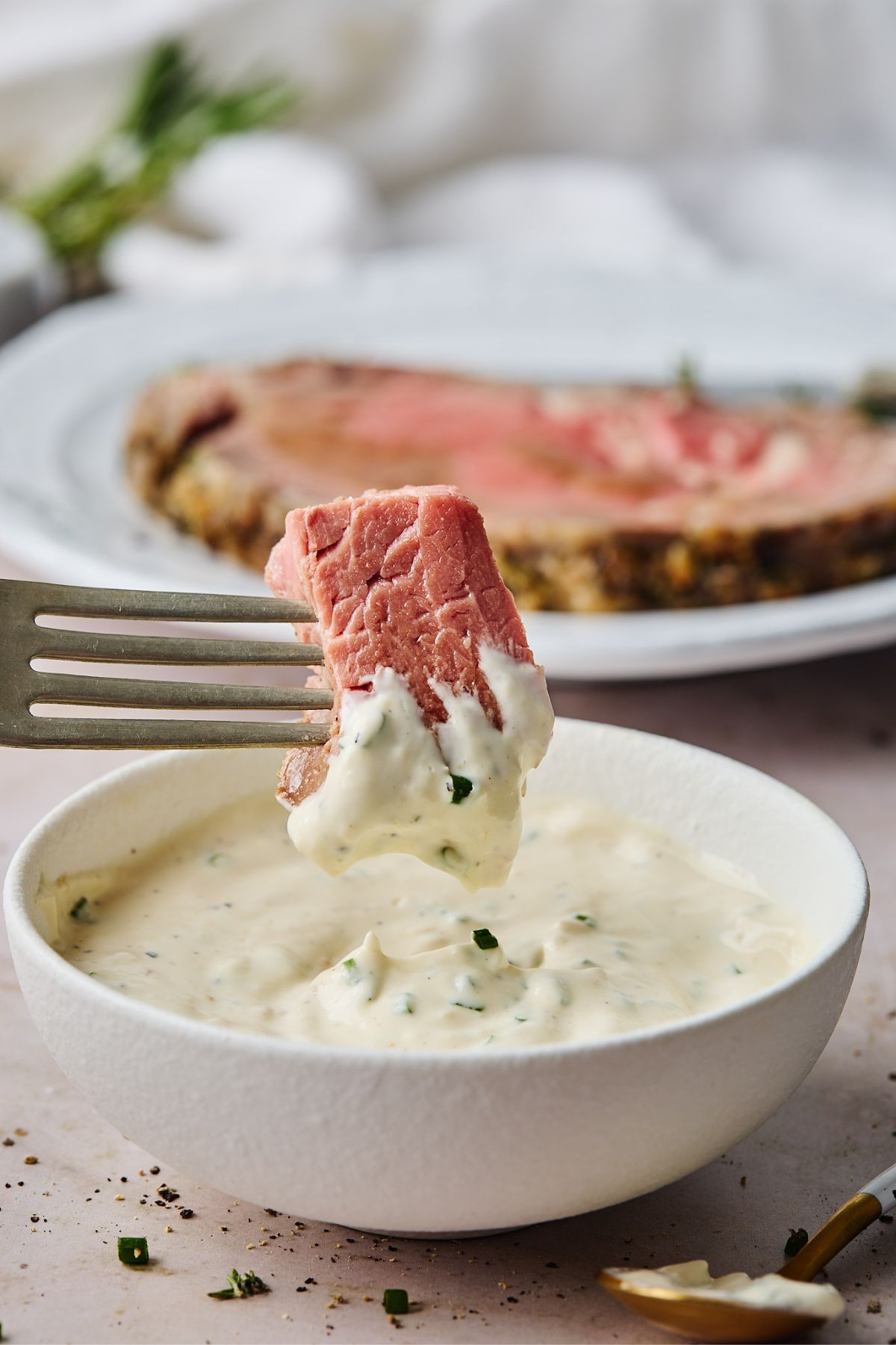 Bite of prime rib being dipped in a small bowl full of the best horseradish sauce recipe