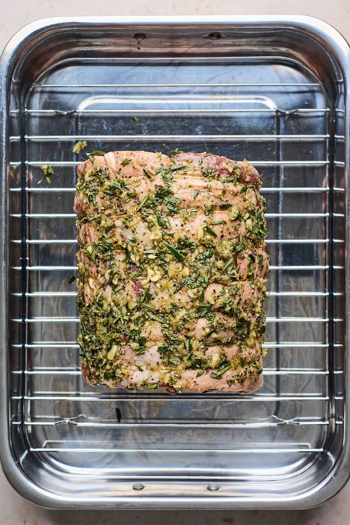 Raw prime rib roast placed on a wire rack inside a roasting pan, fully seasoned and prepared for roasting.