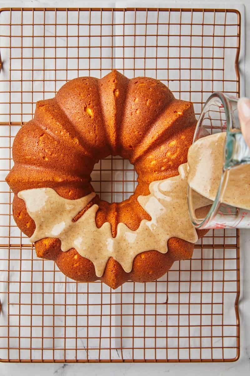 Brown butter glaze being added to pumpkin cake on wire rack.