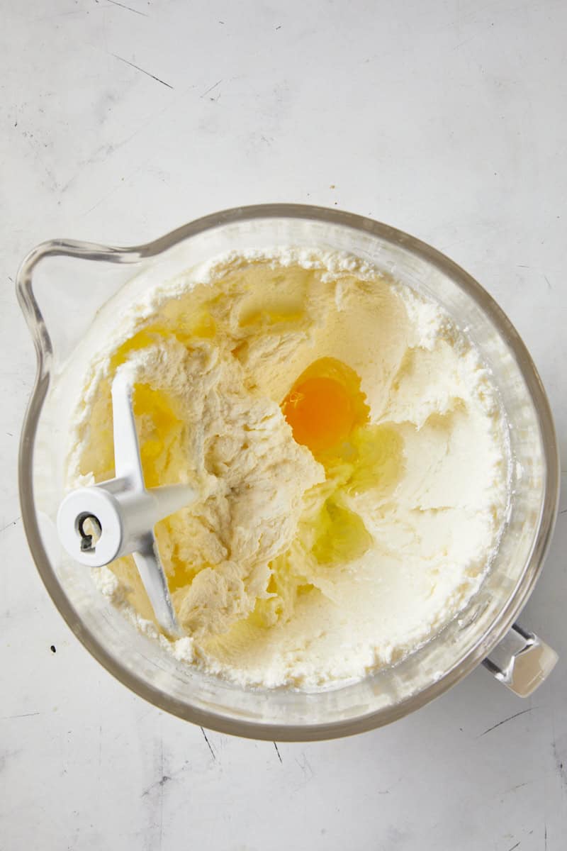 Eggs added to a stand mixer with creamed butter and sugar in a glass mixer bowl