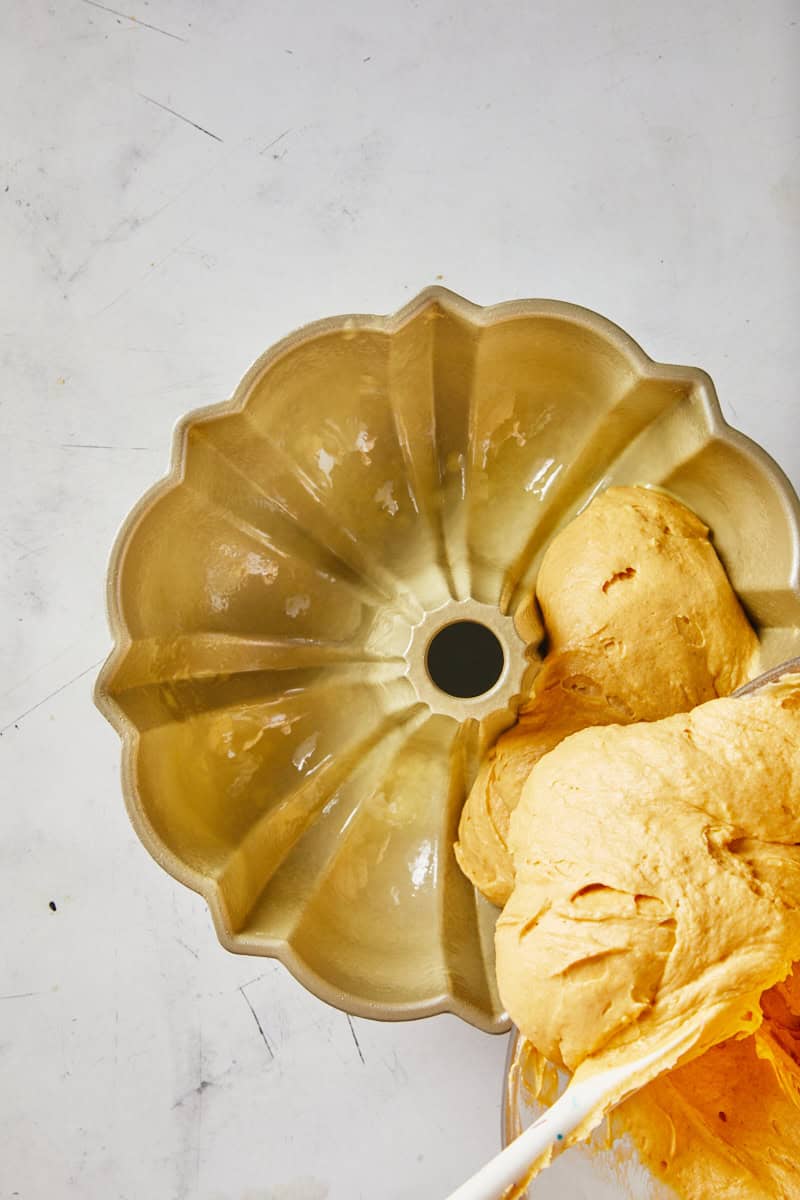 Pumpkin bundt cake batter being poured into a greased pan before baking