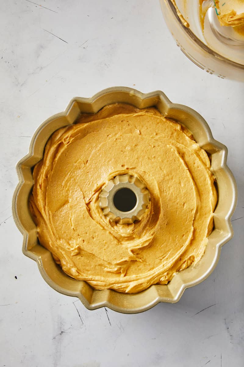 Pumpkin cake batter spread in a cake pan on a white countertop