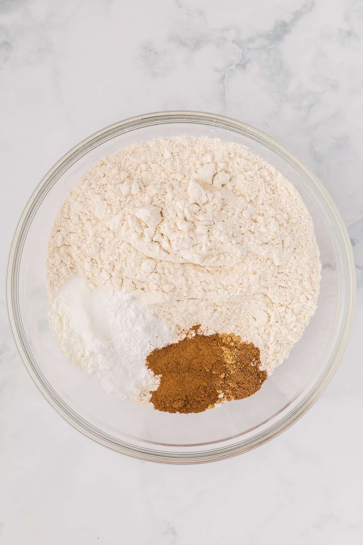 Flour and spices added to a mixing bowl on white countertop