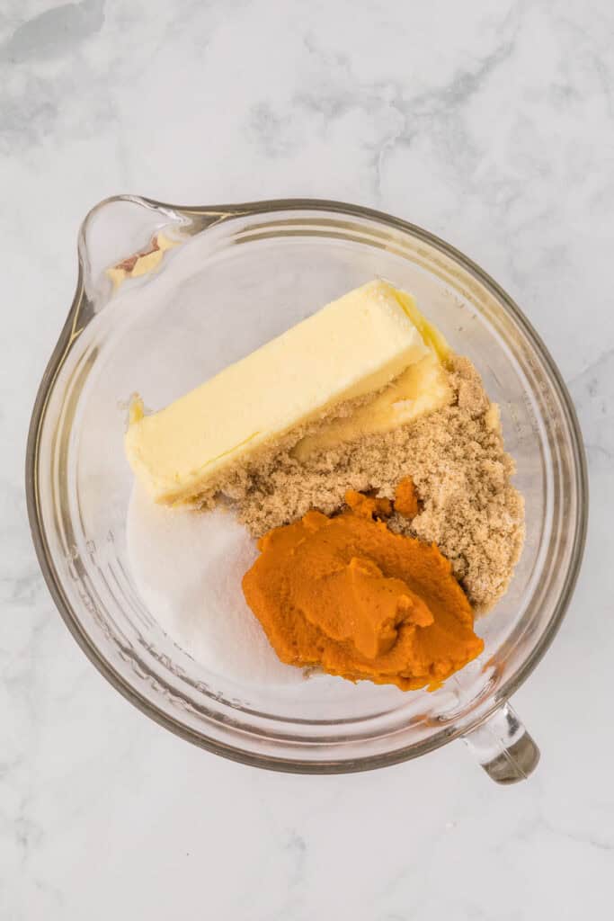 Pumpkin puree, butter and sugars in a mixing bowl on white countertop