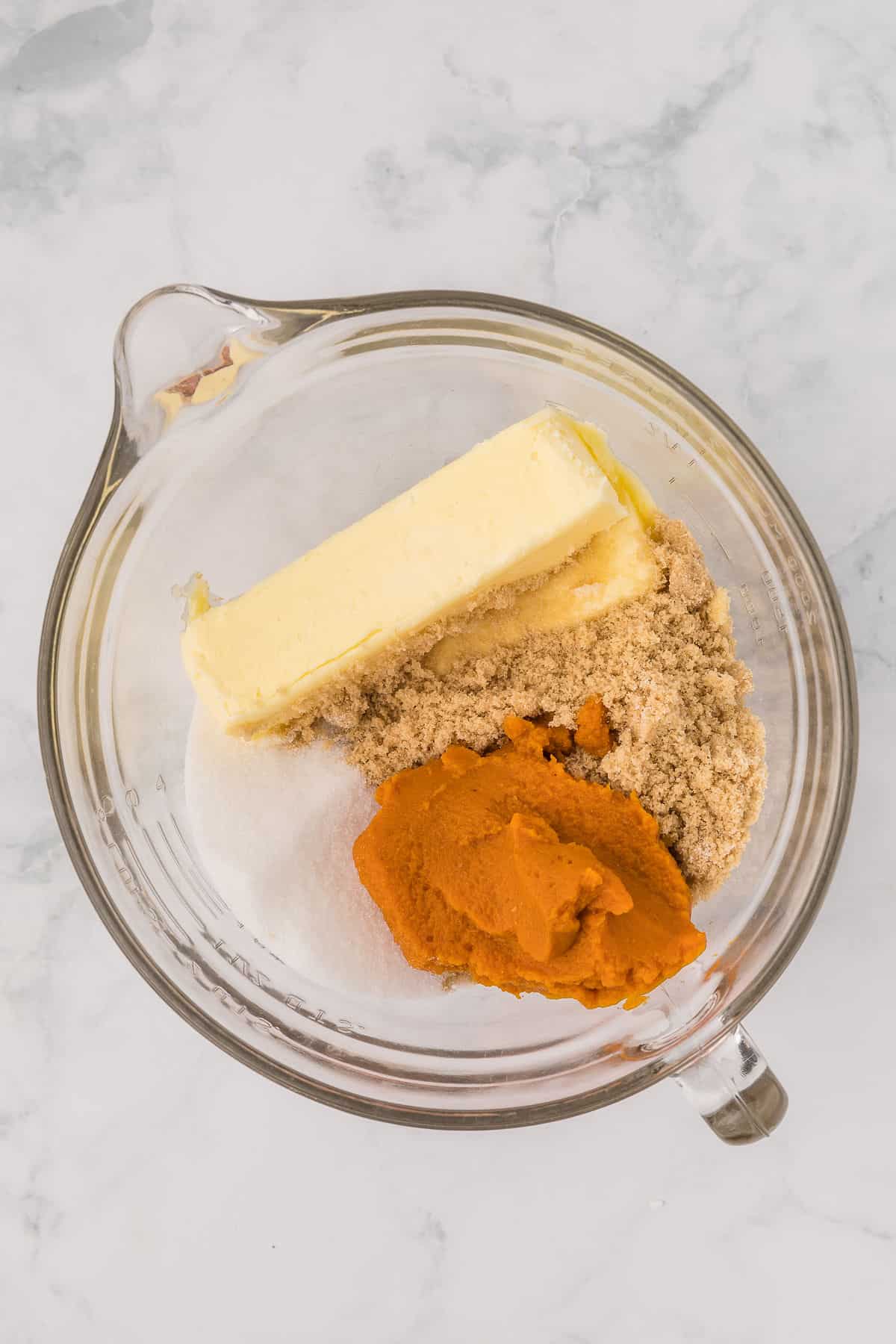 Pumpkin puree, butter and sugars in a mixing bowl on white countertop