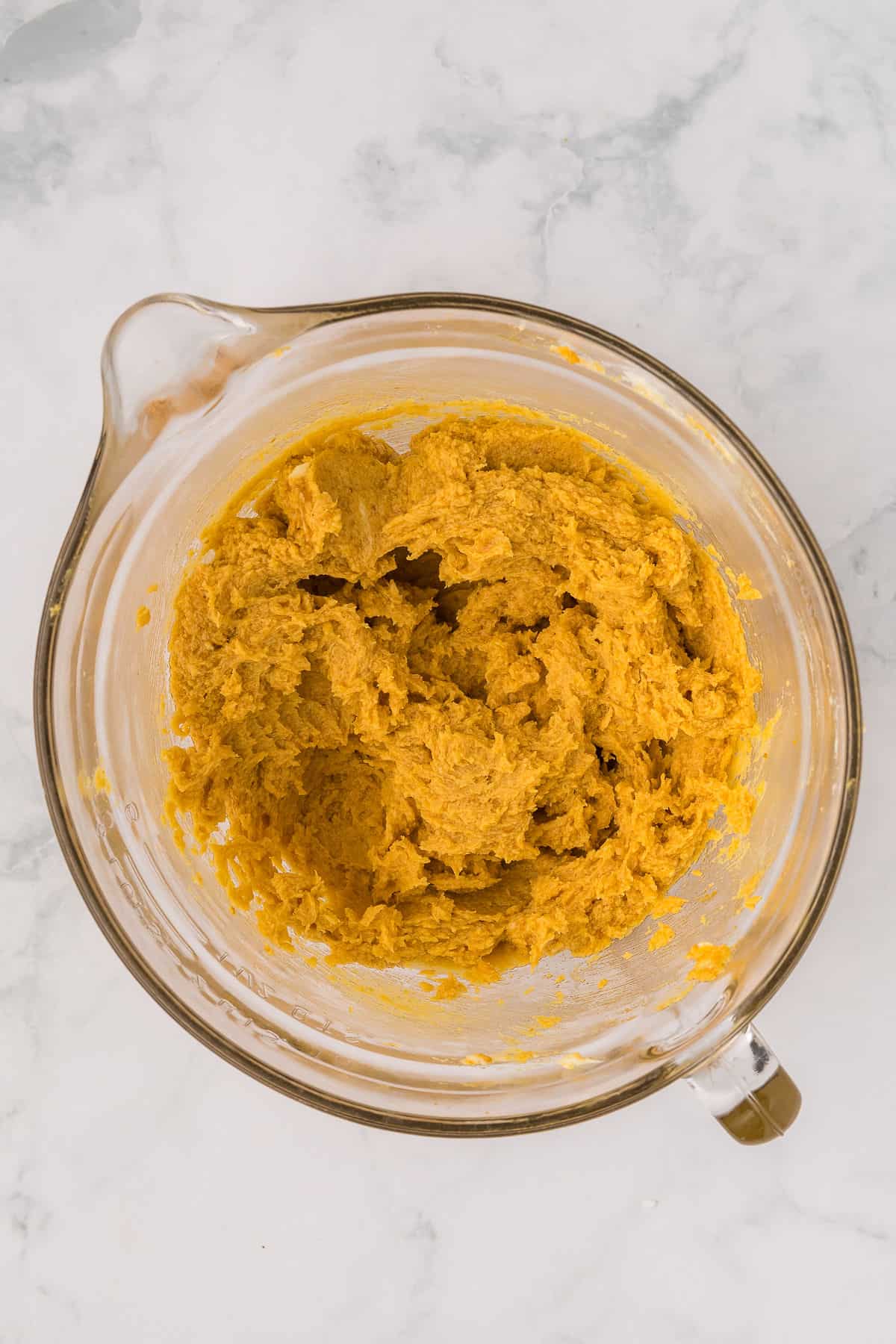 Pumpkin cookie batter mixed in stand mixer bowl until blended on white background