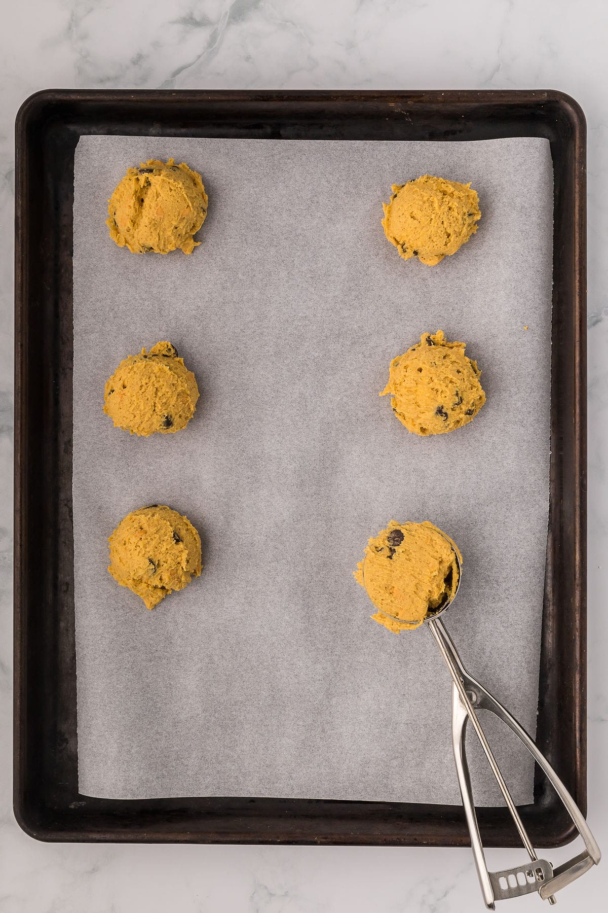 Chocolate chip pumpkin cookie dough being scooped onto a parchment lined baking sheet before baking