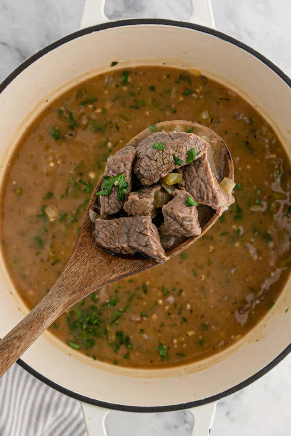 A spoonful of beef tips up over the pot of gravy.
