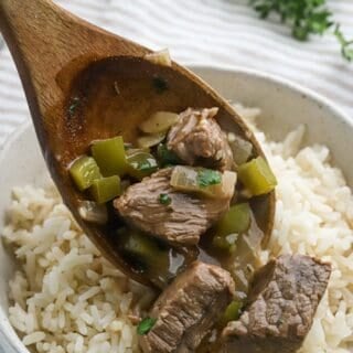 A spoon ladling a serving of beef gravy over a bowl of rice.