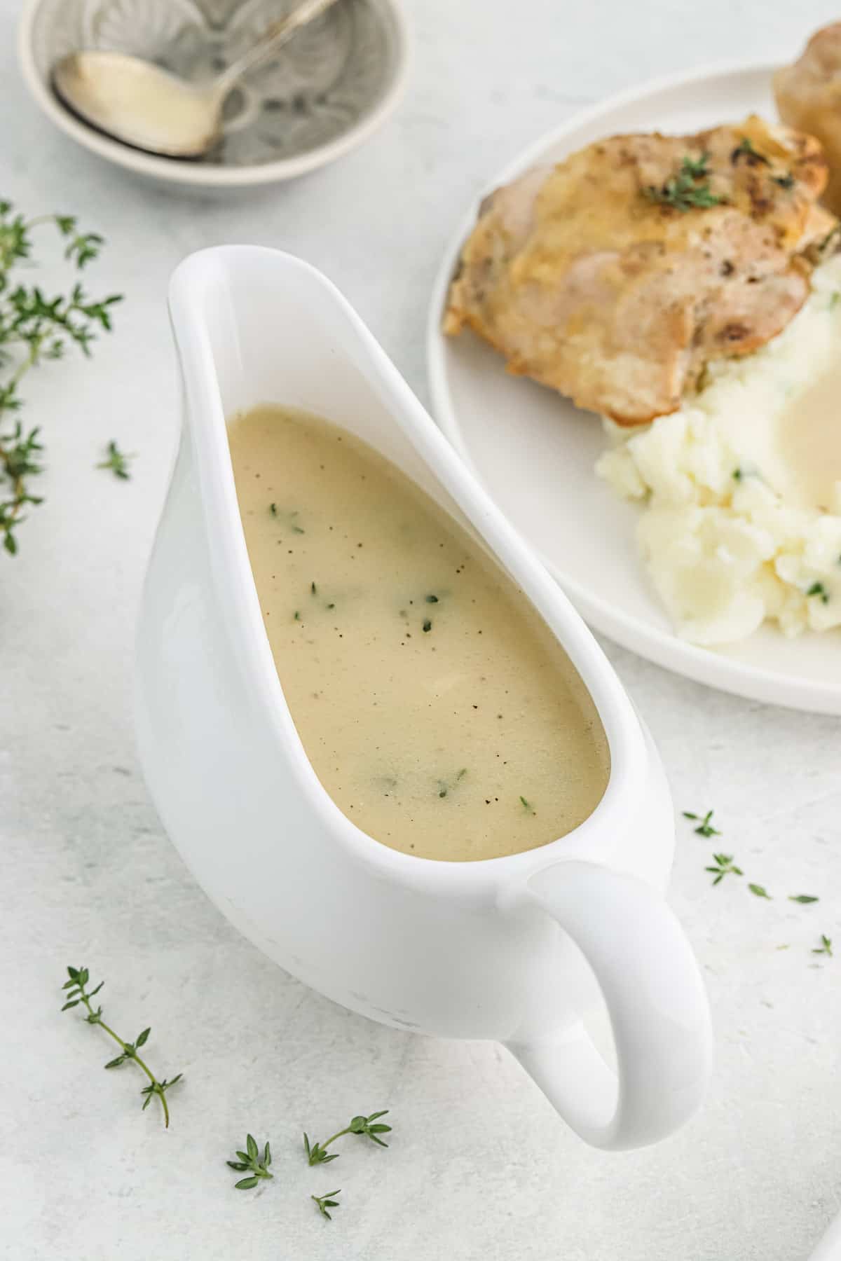 Chicken gravy in a white gravy boat with chicken and mashed potatoes in the background