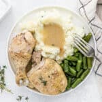 Chicken and gravy in a white plate with mashed potatoes and green beans