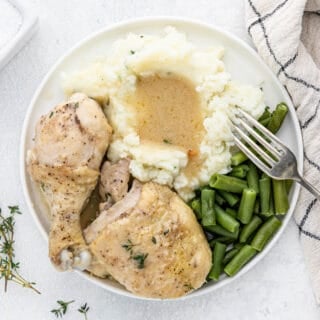 Chicken and gravy in a white plate with mashed potatoes and green beans