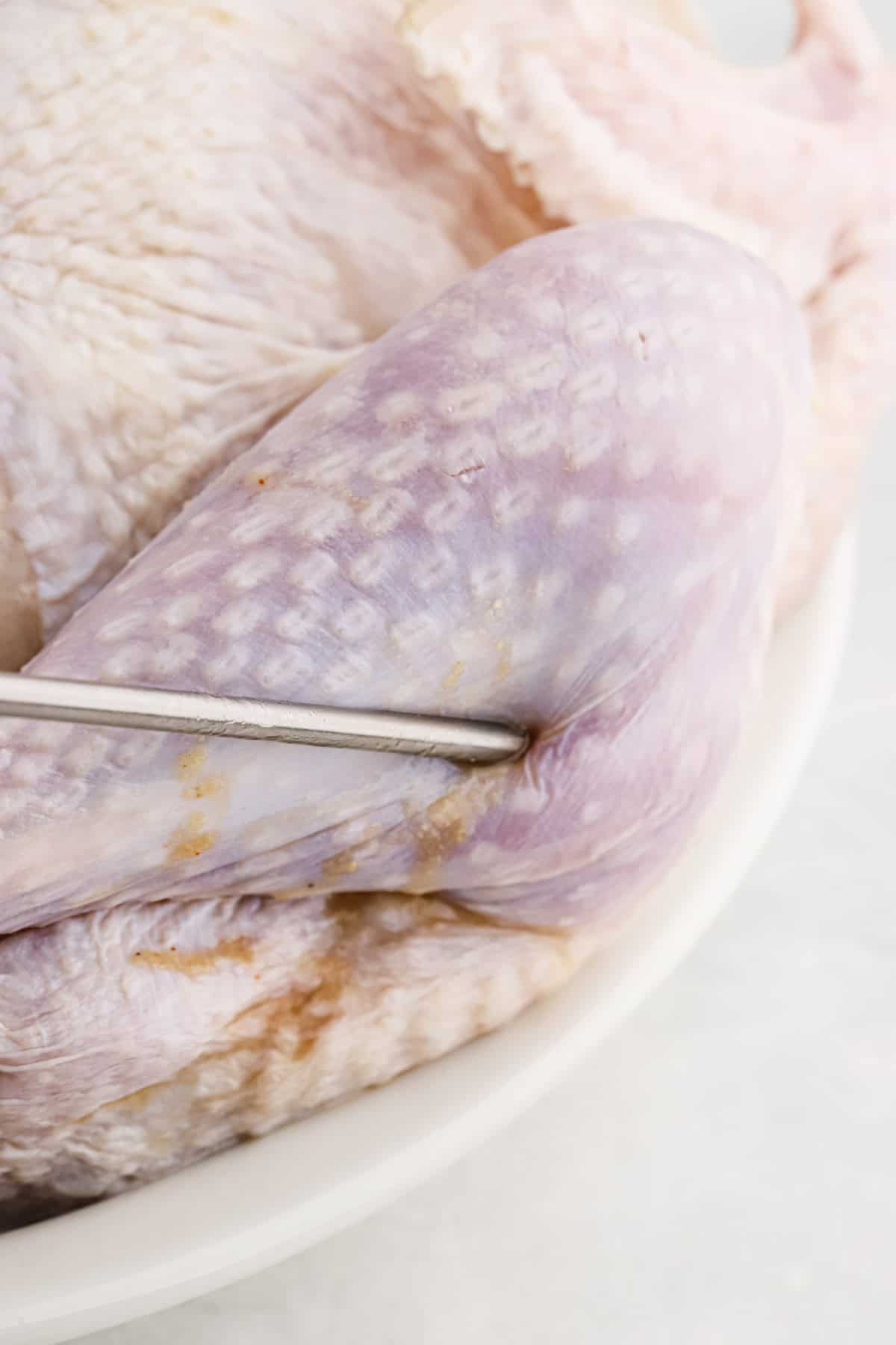 Close-up of a meat injector being inserted into the turkey leg