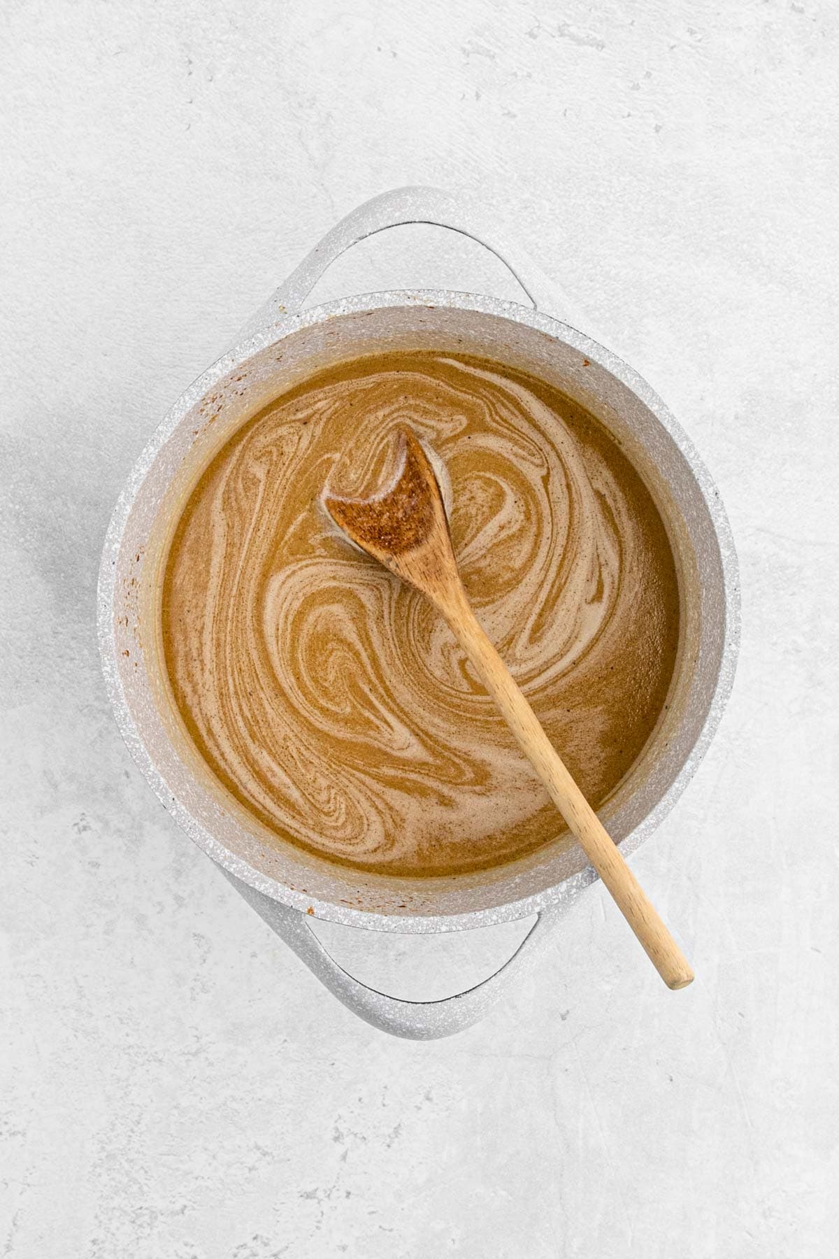 A pot filled with marinade, being stirred with a wooden spoon