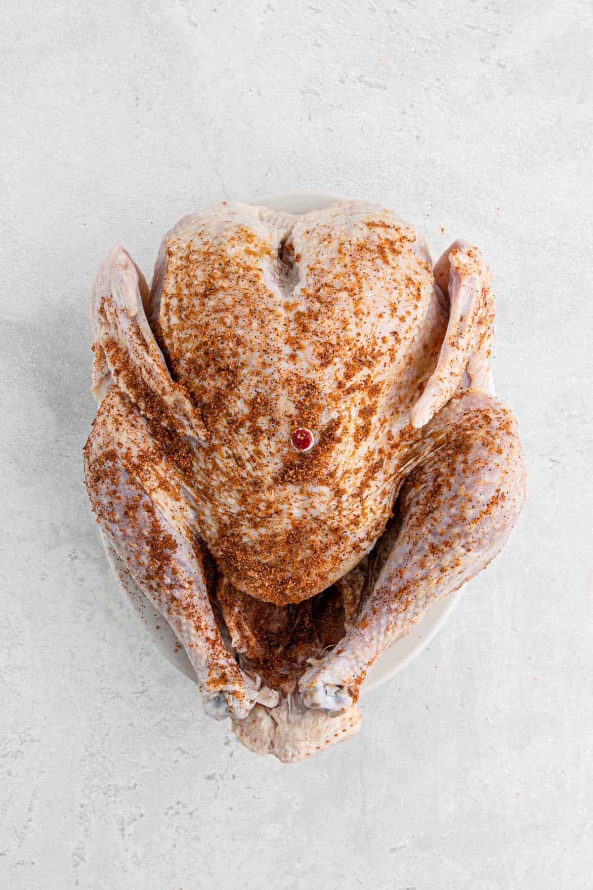 A raw turkey generously coated with seasoning rub